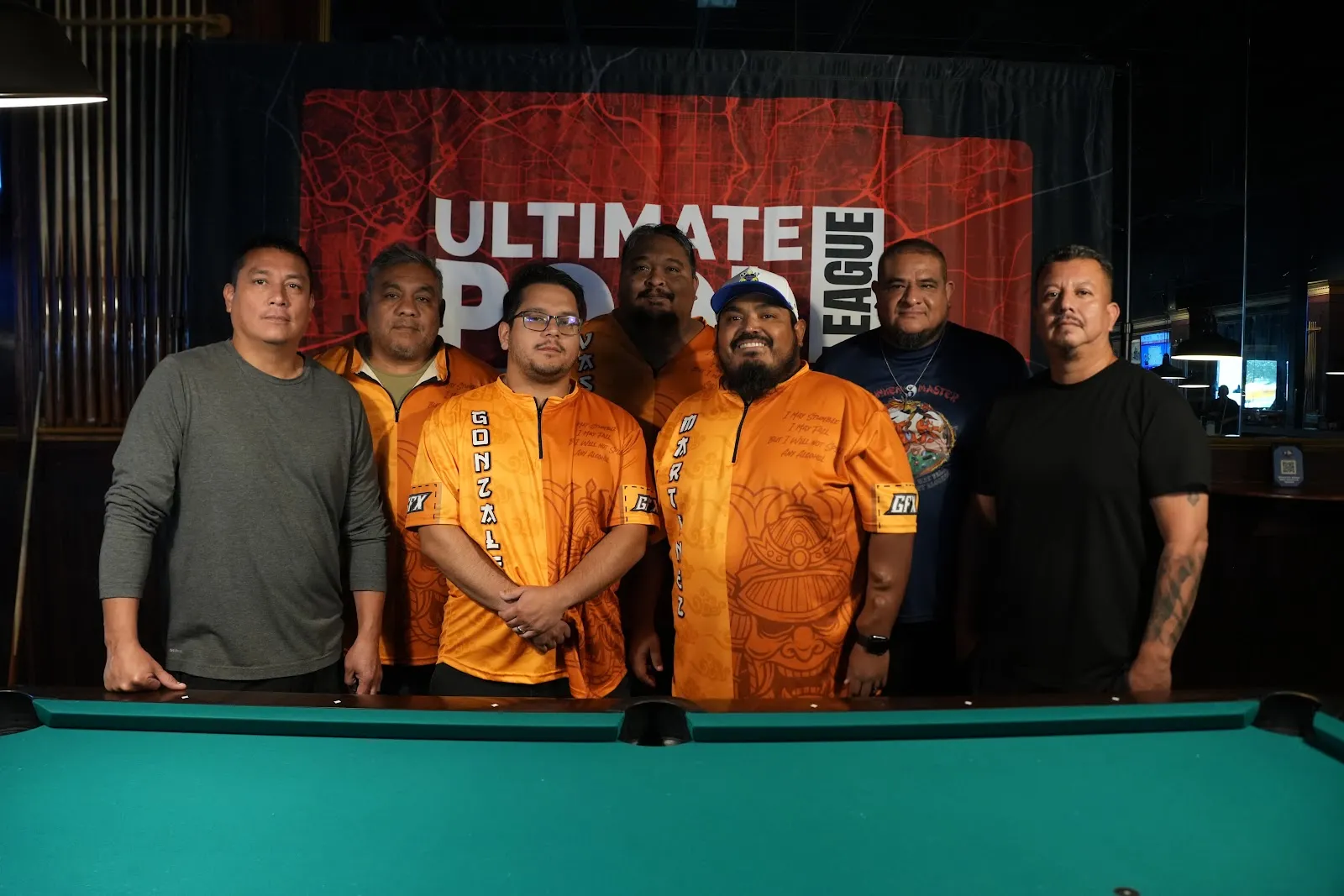 A team in matching shirts posing at the Ultimate Pool League San Antonio banner.